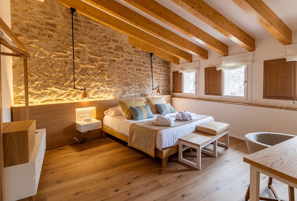 A Forum room with a blue watercolour over the bed, two copper reading lamps, sage and oat cushions and a bare stone wall to one side