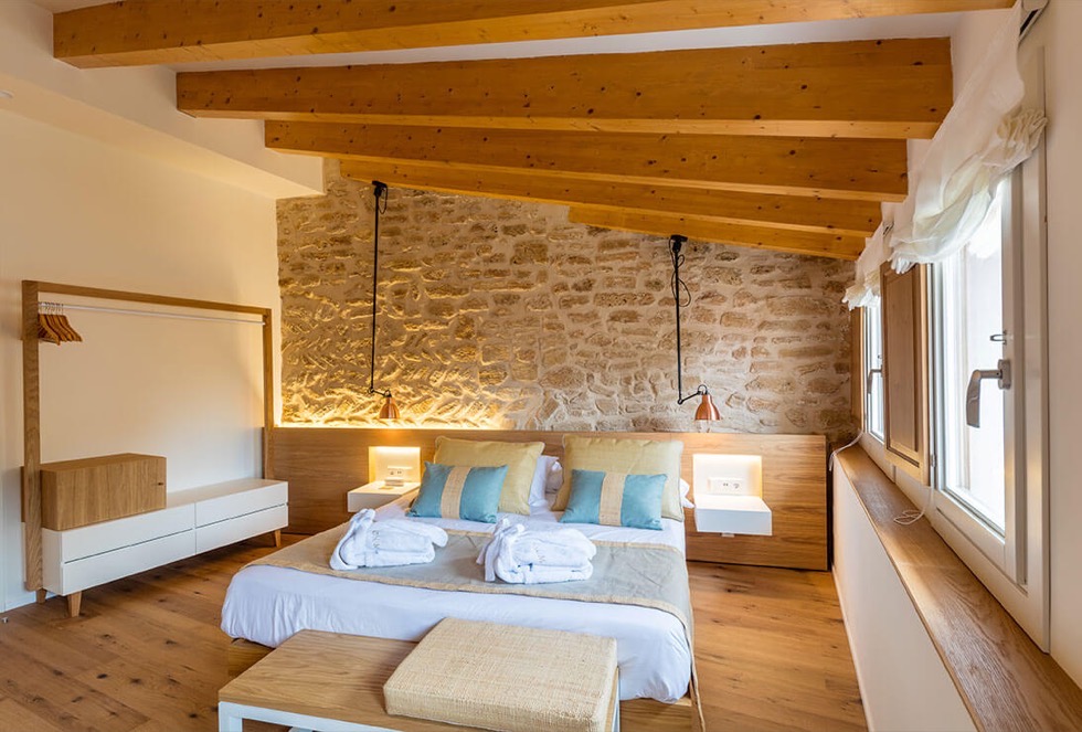 A Forum room under the eaves with a row of small shuttered windows, a desk and chair, sage cushions and a bench at the foot of the bed