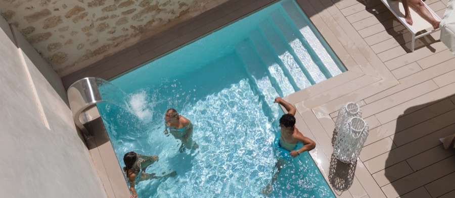 The bright turquoise water of the Forum pool seen from above, steps leading down into it and a water jet running along one wall